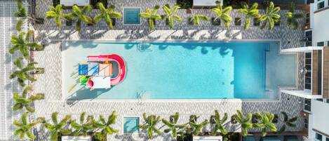 Oversigtsbillede af et hotelpoolområde med et rektangulært pool, flere liggestole og palmer.
