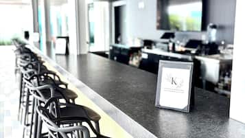 A bar area with a long counter, multiple stools, and a sign.
