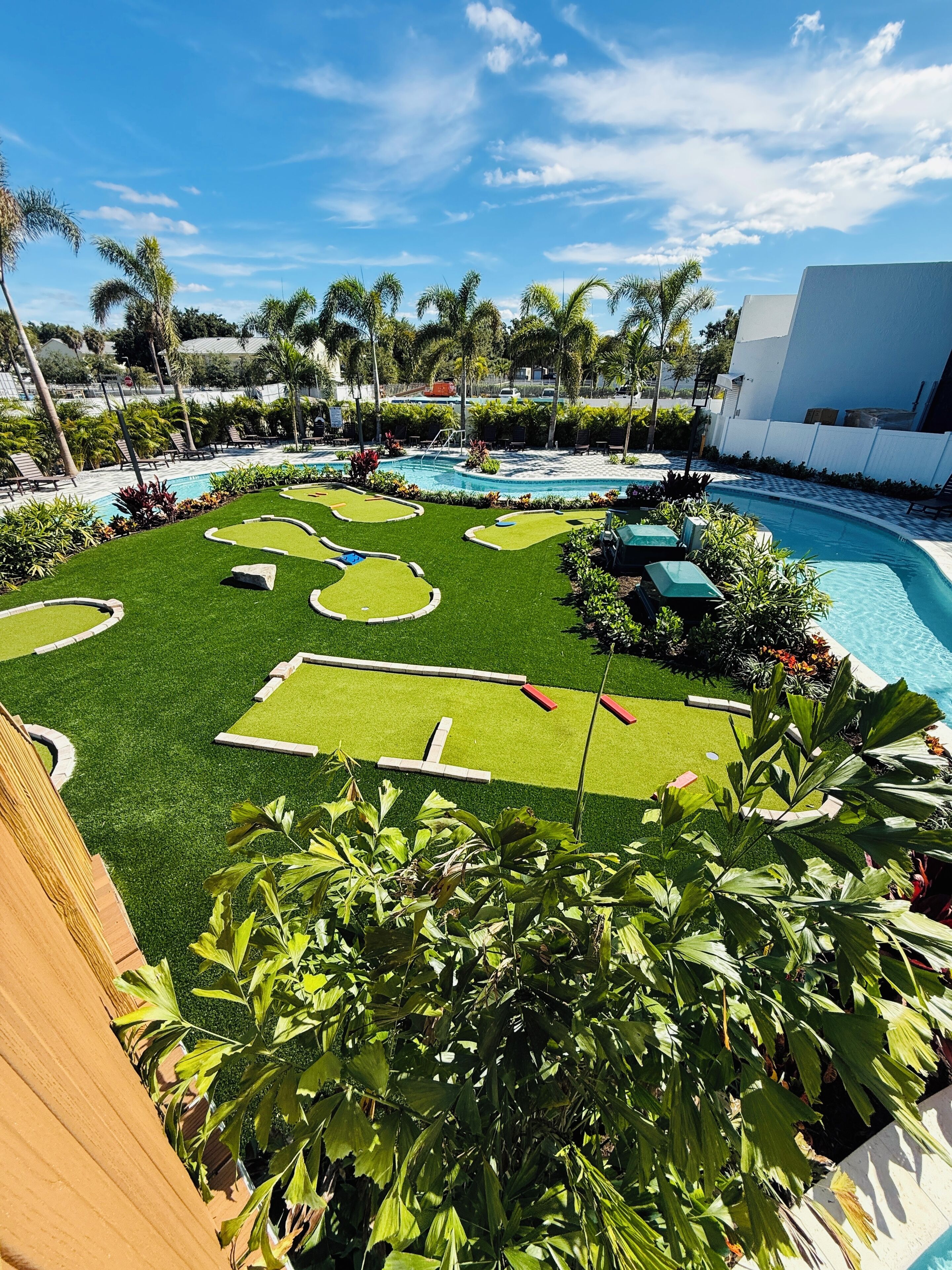 Un área de piscina con césped artificial, palmeras y sillones de descanso.
