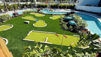 A pool area with artificial grass, palm trees, and lounge chairs.