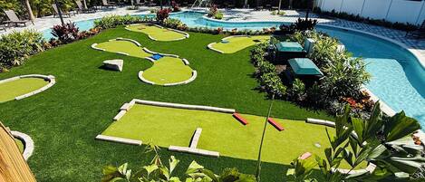 A pool area with artificial grass, palm trees, and lounge chairs.