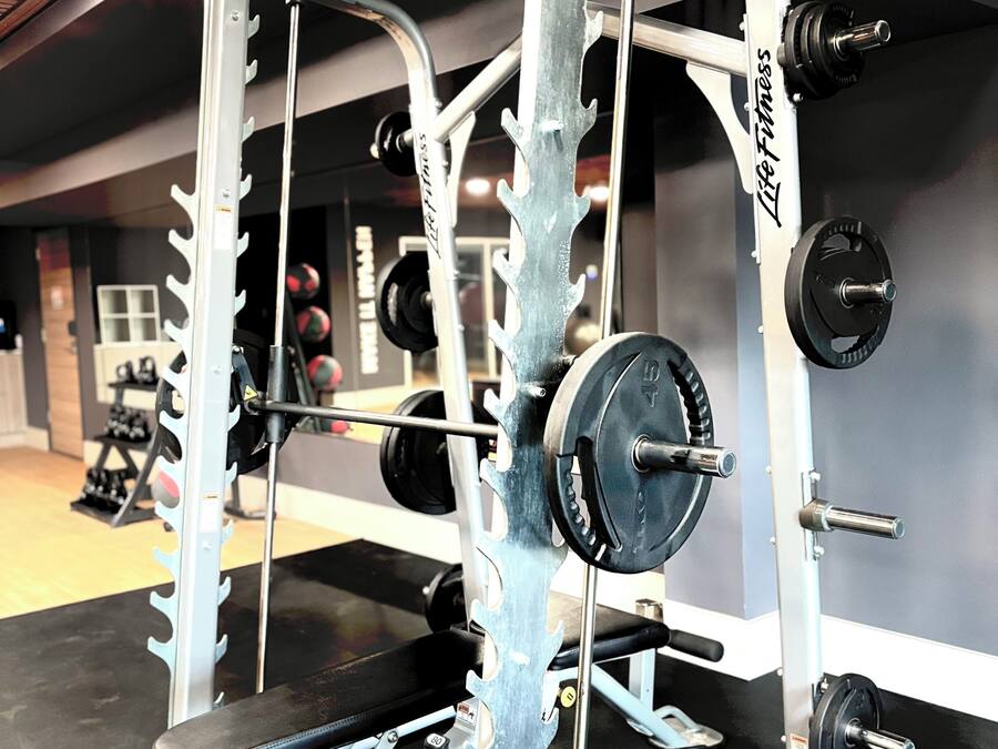 Un gimnasio con una estructura para sentadillas, barra, discos de pesas y un banco.