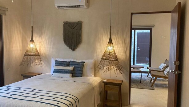 Ein Schlafzimmer mit einem Bett, Nachttischen, einer Wanddekoration aus Makramee und einer Klimaanlage.