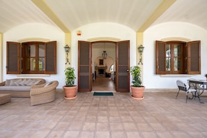 A covered patio area with a sofa, a dining table, and potted plants.
