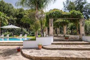 A pool area with lounge chairs, a pergola, and potted plants.