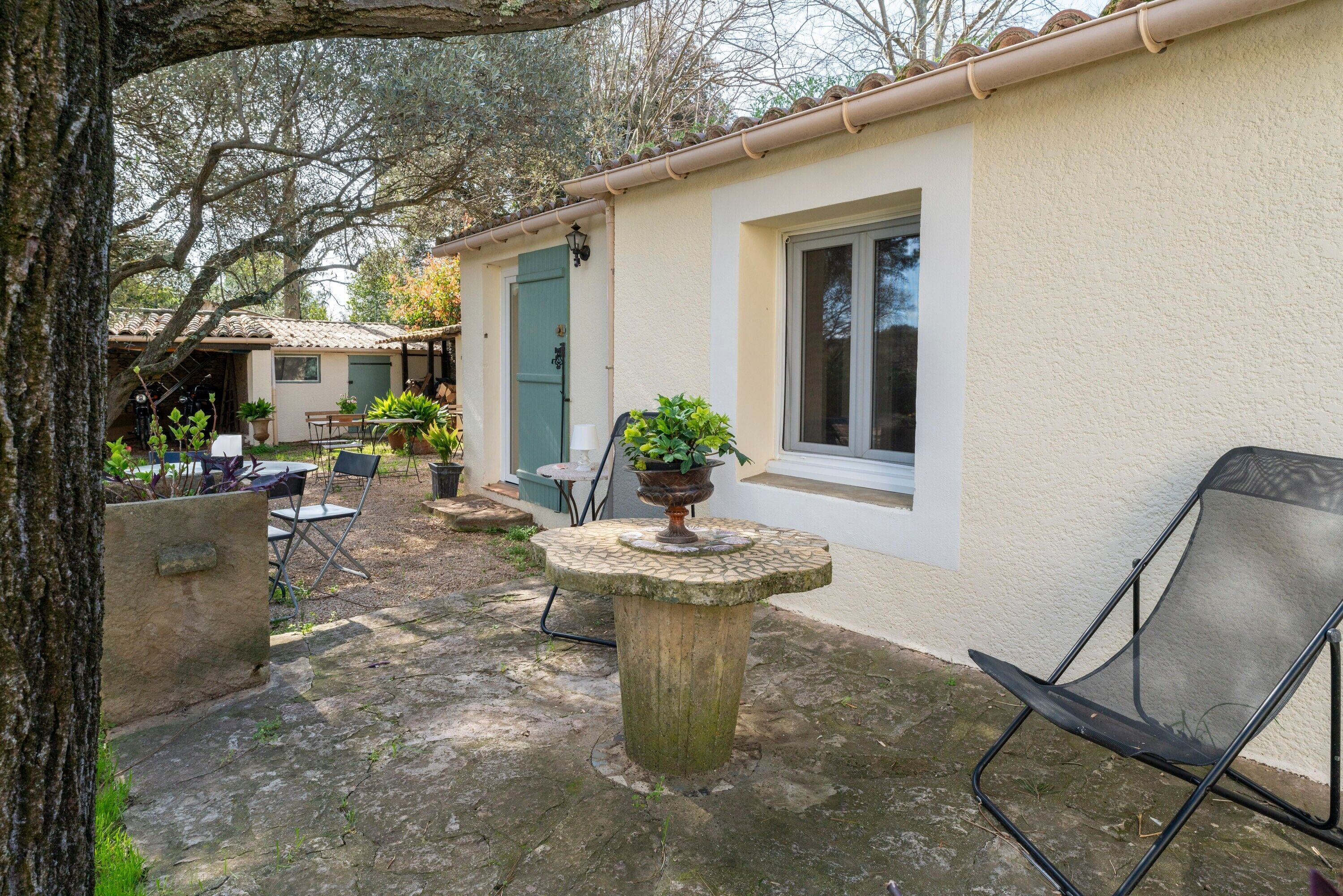Une cour avec une table en pierre, des sièges extérieurs et un bâtiment doté d’un toit en tuiles.