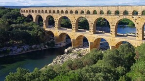 Un puente de piedra con varios arcos que cruza un río, rodeado de vegetación.