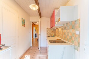 Un pasillo estrecho que lleva a una cocina con armarios blancos, salpicadero de azulejos y techo de madera.