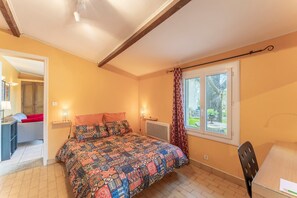 Un dormitorio con cama, ventana con cortinas, una silla y un escritorio.