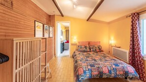 Un dormitorio con cabecera de madera, colcha estampada, radiador y ventana con cortinas.