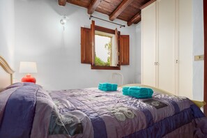 A bedroom with a bed, a window with wooden shutters, a bedside lamp, and a wardrobe.
