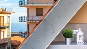 En balkong med en krukväxt och en lykta, med utsikt över ett bostadsområde med byggnader och en klar himmel.