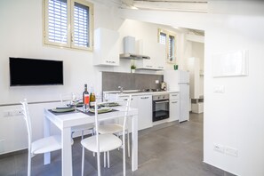 Une cuisine moderne avec des meubles blancs, un téléviseur à écran plat et un coin repas avec des chaises blanches.