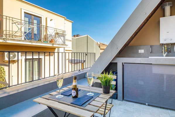 A balcony with a table, two wine glasses, a bottle, and a potted plant.