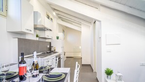 Ett modernt kök med vita skåp, ett matbord för fyra personer och utsikt över det intilliggande matrummet.