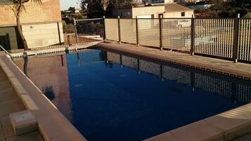 Una piscina rectangular con solárium empedrado, rodeada por una valla y palmeras.