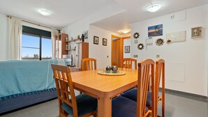 A dining area with a wooden table, blue cushioned chairs, a sofa with a blue cover, and a view through a large window. - Apartment "Deltebre Riu" with Shared Pool & Wi-Fi (Deltebre)