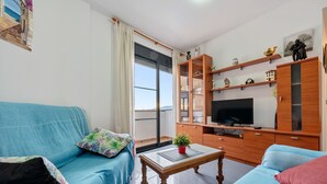 A living room with a sofa, a coffee table, a TV, and a wooden cabinet with shelves. - Apartment "Deltebre Riu" with Shared Pool & Wi-Fi (Deltebre)