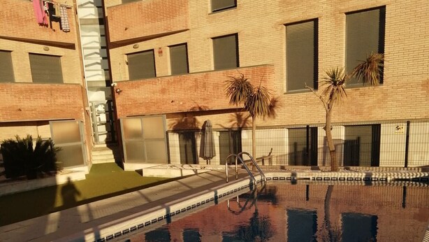 A swimming pool with a tiled deck, surrounded by a building with multiple windows and balconies. - Apartment "Deltebre Riu" with Shared Pool & Wi-Fi (Deltebre)