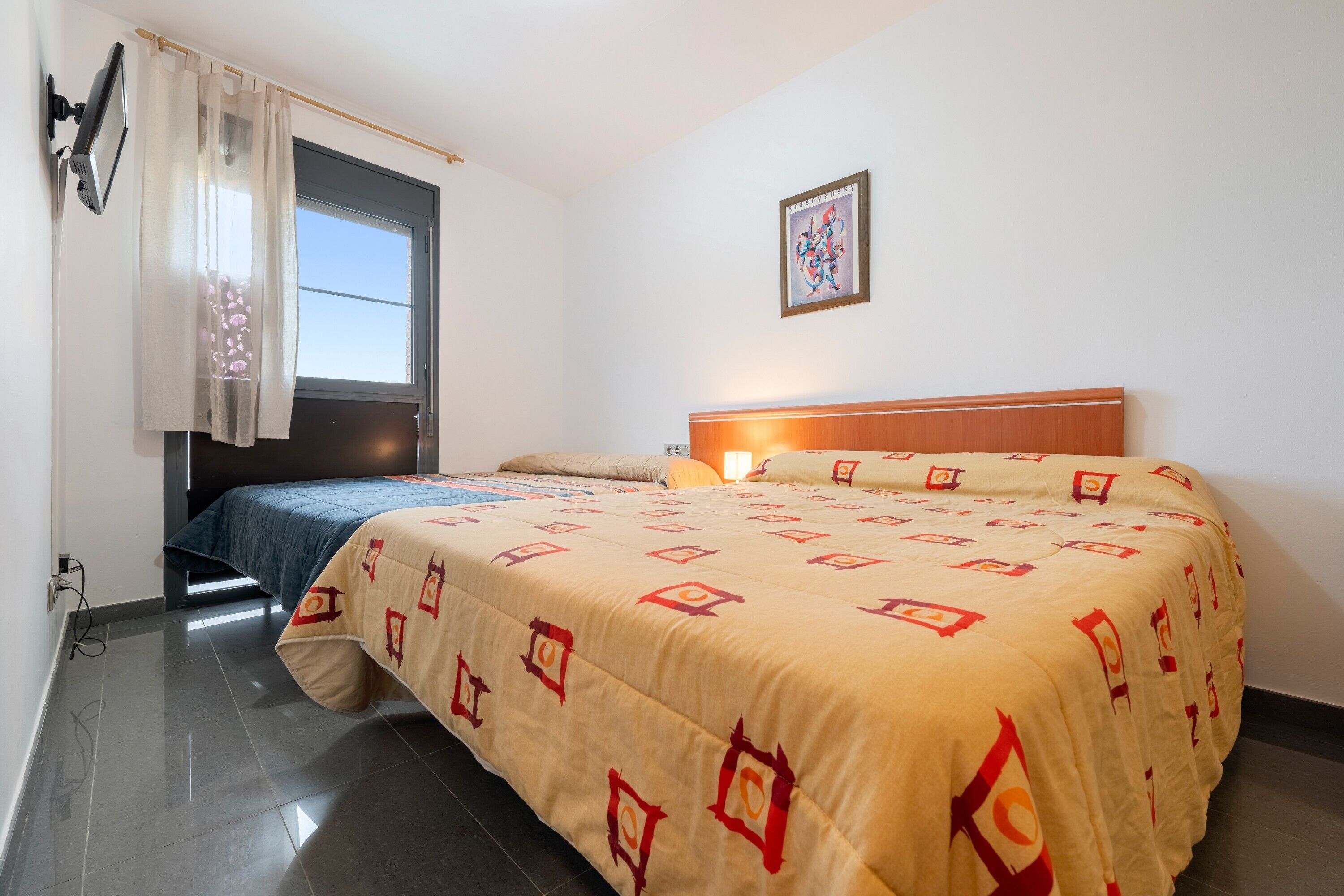 Un dormitorio con cama, ventana con cortinas, una obra de arte en la pared y una lámpara de noche.