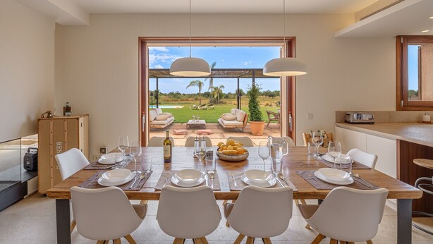 A dining area with a view of a golf course, a wooden table set for four, and a kitchen area with a countertop and a sink.
