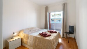 A bedroom with a bed, a nightstand with a lamp, a chair, and a window with curtains. - Holiday Apartment "Portimão" with Mountain View, Shared Pool & Wi-Fi (Portimão)