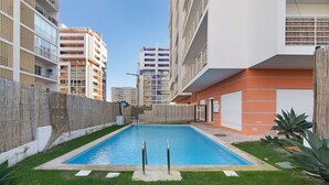 A swimming pool surrounded by a grassy area, with a building featuring balconies and a white facade in the background. - Holiday Apartment "Portimão" with Mountain View, Shared Pool & Wi-Fi (Portimão)