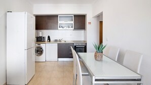 A modern kitchen with a dishwasher, microwave, and oven, a dining table with chairs, and a washing machine. - Holiday Apartment "Portimão" with Mountain View, Shared Pool & Wi-Fi (Portimão)