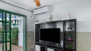 A modern living room with a large flat-screen TV, a built-in air conditioner, and a green-framed sliding door leading to an outdoor area. - Vacation Apartment 'Dunaflor Gemelo 3' with Shared Pool, Wi-Fi and Air Conditioning (San Bartolomé de Tirajana)