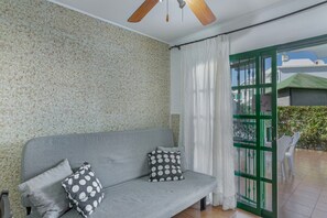 A room with a grey sofa, two patterned pillows, a ceiling fan, and a green door leading outside.