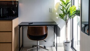 A bedroom with a bed, a desk with a chair, a potted plant, and a large window. - Olive Apartments (Miami)