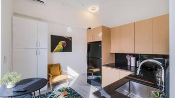 A modern kitchen with a black countertop, stainless steel sink, and wooden cabinets. There is a yellow chair and a potted plant on the floor.