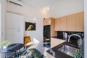 A modern kitchen with a black countertop, stainless steel sink, and wooden cabinets. There is a yellow chair and a potted plant on the floor. - Olive Apartments (Miami)