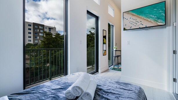 A modern hotel room with a large bed, a balcony with a view of the city, and a TV on the wall. - Olive Apartments (Miami)