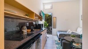A compact kitchen with modern appliances, a dining area with a small table and chairs, and a sofa in a living space. - Olive Apartments (Miami)