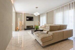 A modern living room with a sofa, a flat-screen TV, a fireplace, and a ceiling light fixture.