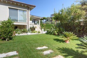 A modern house with a well-maintained lawn, a covered porch, and a variety of plants.
