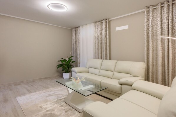 A modern living room with a beige sofa, a glass coffee table, a potted plant, and a ceiling light.