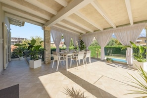 An outdoor patio with a table and chairs, surrounded by potted plants and a view of the pool.