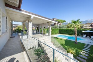 Une maison moderne dotée d’un balcon en verre, d’une piscine et d’un jardin bien entretenu.