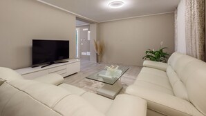 Ein modernes Wohnzimmer mit Fernseher, Glastisch und zwei weißen Sofas.