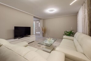 Un salon moderne avec un téléviseur à écran plat, une table basse en verre et deux canapés blancs.