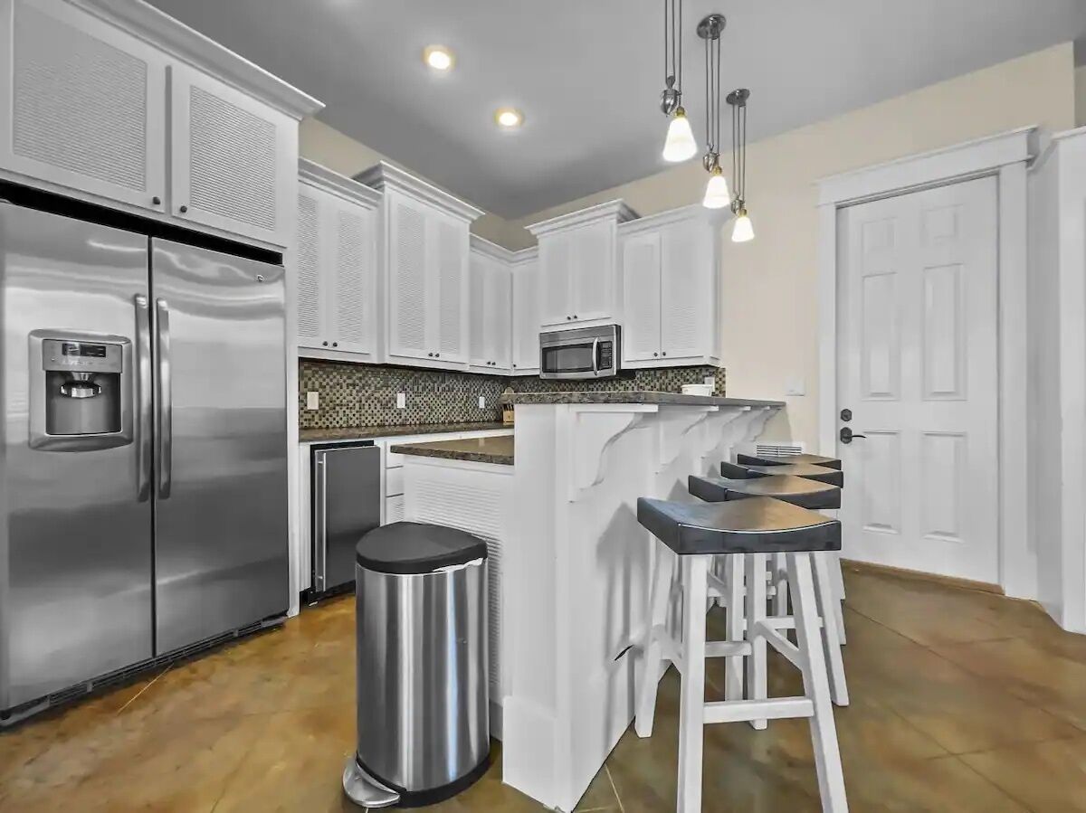 Una cocina moderna con armarios blancos, electrodomésticos de acero inoxidable, microondas integrado y una zona de bar con taburetes.