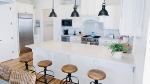 Une cuisine moderne avec des meubles blancs, un îlot central doté de tabourets, une cuisinière et des luminaires suspendus.