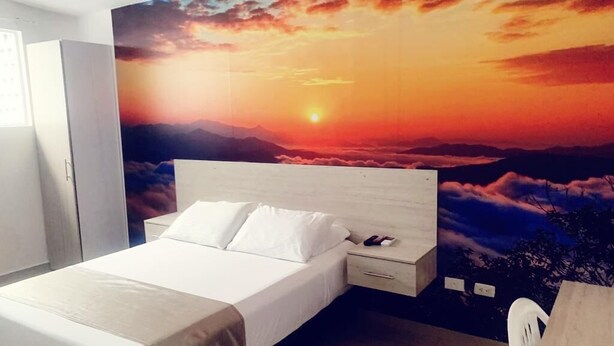 Un dormitorio con cama, mesita de noche y un mural en la pared que muestra un atardecer sobre montañas.