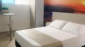 Una cama bien hecha con ropa blanca en una habitación con un cuadro grande de un atardecer en la pared.