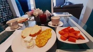 Desayuno con tostadas, tortilla, fruta en cubos en platos, además de tazas de café y un vaso de bebida roja.