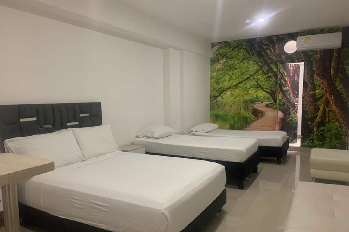 A hotel room with three beds, a desk, and a mural of a forest scene.