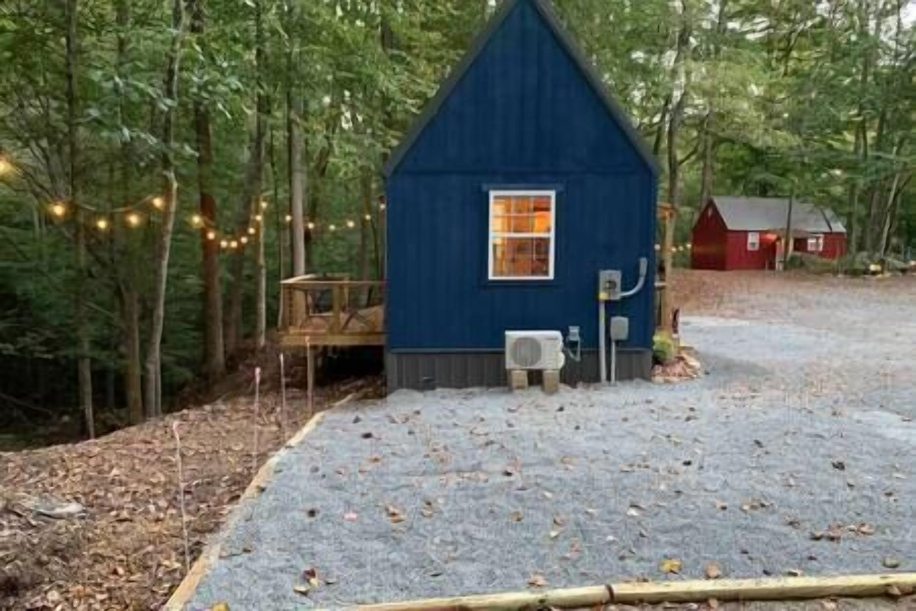 A small blue cabin with a window, surrounded by trees and a gravel path.