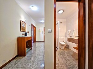 Ein Flur mit einem Holztisch und einem gerahmten Bild an der Wand, der zu einem Badezimmer mit Toilette, Waschbecken und Handtuchhalter führt.